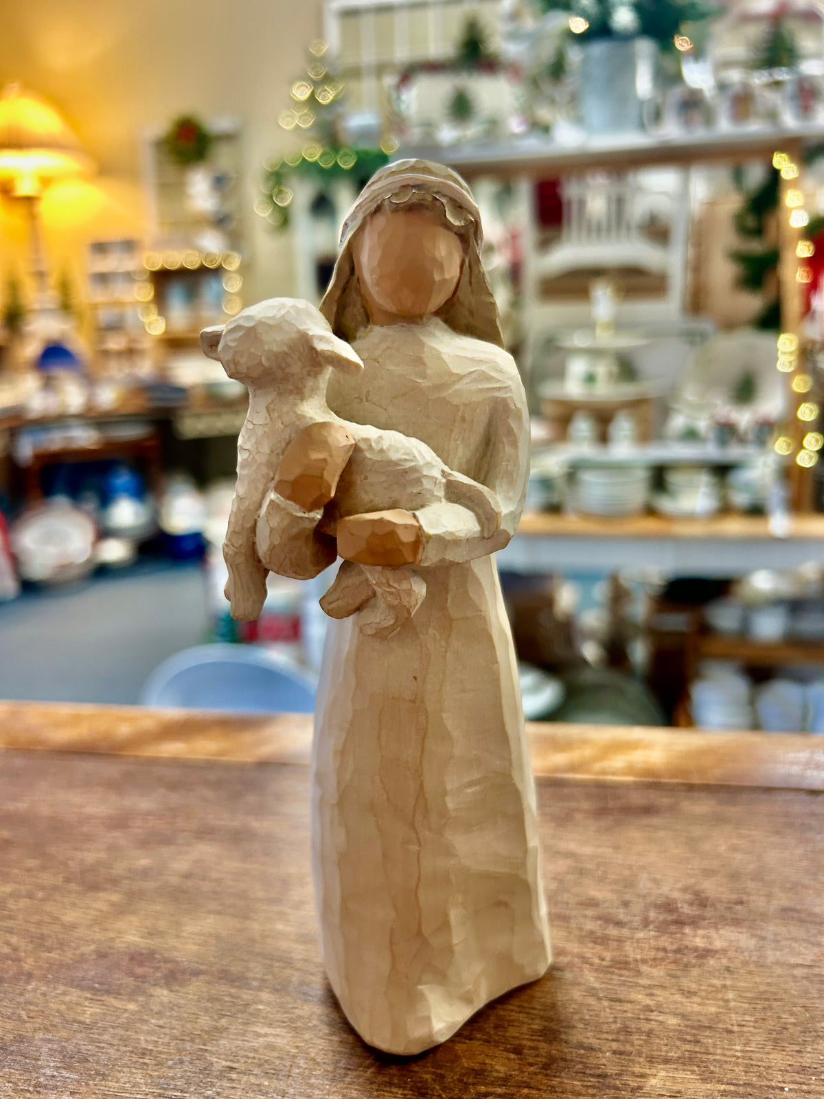 Cream nativity girl figurine holding sheep, standing on wooden tabletop