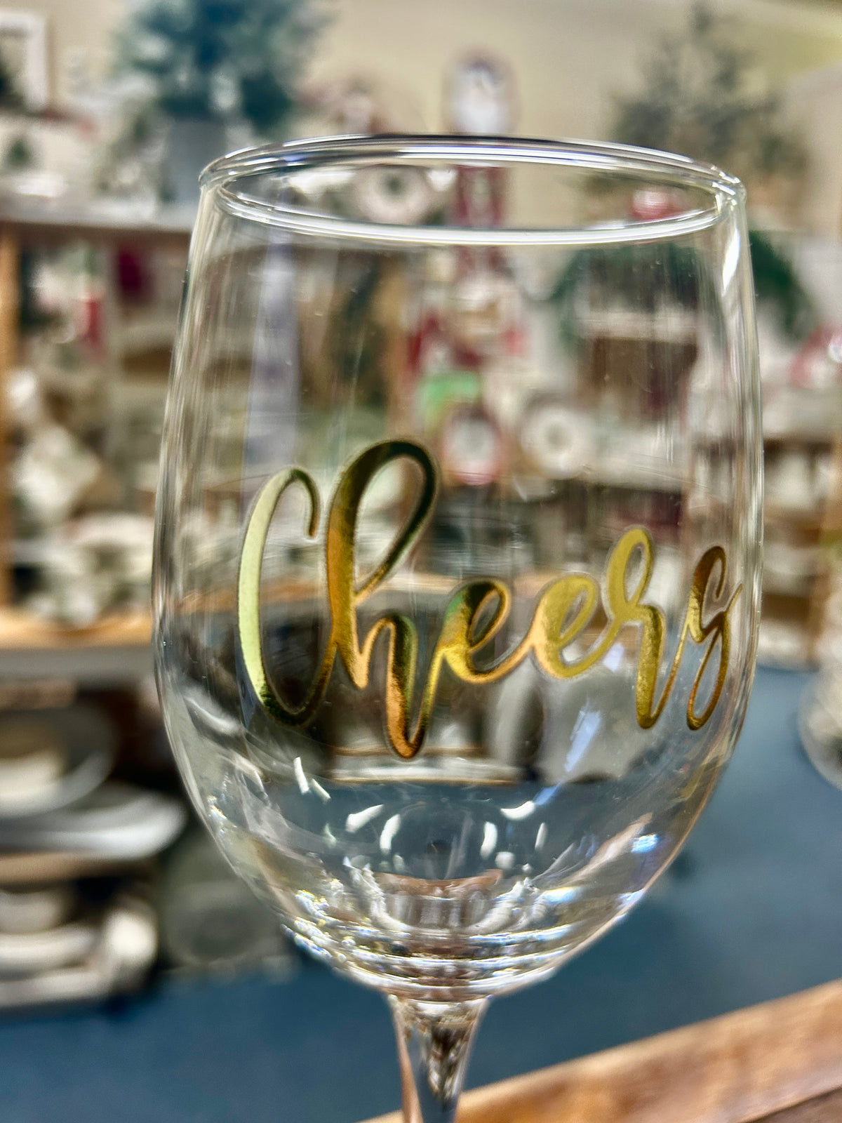 Clear wine glass showing gold “Cheers” lettering on the bowl