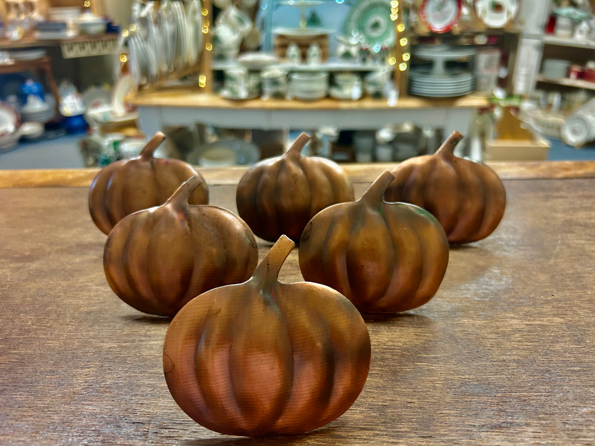 Set of copper pumpkin-shaped napkin rings, clustered on a tabletop