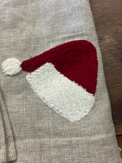 Folded linen-style napkin with red Santa hat applique and white pom, angled close-up