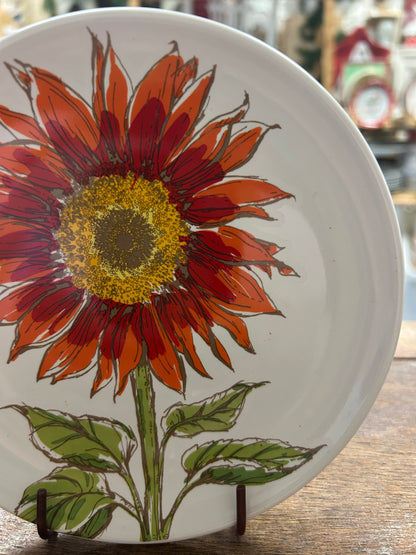 White sunflower plate with red-orange flower and green leaves on front