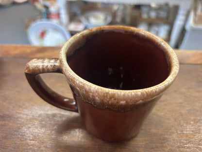 Brown ceramic mug on a table with speckled rim and visible interior glaze